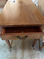 Photo showing the full top and front of a wooden end table with an open drawer, revealing the drawer interior and metal pull handles.