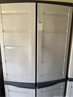 Full front view of large white plastic utility cabinet with black base and handles showing closed doors.