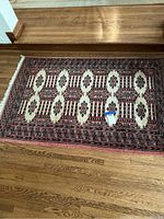 Full view of the Persian style rug laid out flat on a wooden floor near stairs, showing the full pattern and fringe edges.