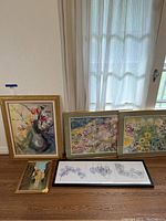 Four framed pictures arranged on floor against wall, showing various floral paintings and botanical leaf line art