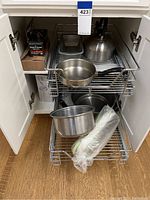 Stainless steel pots, metal tea kettle on kitchen wire shelves inside cabinet, wrapped kitchen utensil, wire rack shelves.