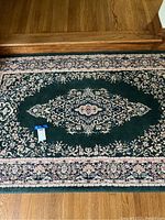 Close-up photo of the central medallion and floral pattern of the dark green rug.