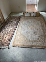 Two flat area rugs laid out on floor with two additional rolled rugs, showing pattern and size distinctness.