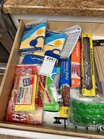 Drawer cluttered with kitchen and household items including sponges, wipes, wax paper, food storage bags, and more