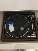 Photo of Dual turntable showing platter, tonearm, and brand label with remote control on platter.