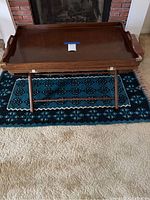 Wooden folding table with lift-off serving tray on top of decorative blue rug, positioned near fireplace.