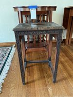 Front-left angle of two small tables and part of the wine rack showing wood finishing and carved details on one table