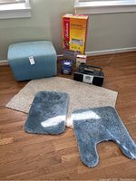 Lot items arranged on wooden floor: rugs, ottoman, CD player, boxes for heater and heat pad.