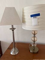 Front view of both lamps showing the metal base lamp with beige lampshade on the left and glass orb lamp with white shade on the right.