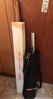 Photo of boxed Stanrite aluminum artist easel and black carrying bag leaning against wooden wall.