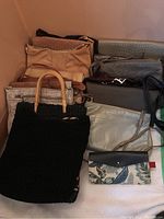 Multiple purses and clutches in various sizes and colors including black woven bags, leather, and fabric clutches arranged together