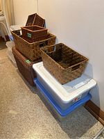 Six wicker baskets stacked on top of six plastic storage bins with lids, blue and white color visible.