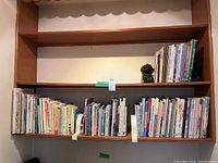 Shelf with multiple books on art and painting, with a dark stoneware bookend on the right side and a plastic bookend on the left.