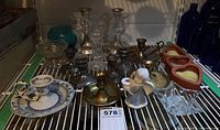 Wide view of assorted candle holders on shelf including glass, brass, ceramic, and metal heart shapes