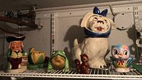 Photo showing the entire collection from left to right: Tommy jug, frog figures, dog cookie jar, squirrel, and bird figurine on shelf in basement.