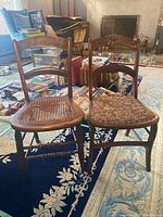 Photo showing two mismatched wooden dining chairs side by side on a dark blue rug with white floral pattern. One chair has a cane seat that is damaged; the other has a brown floral fabric seat.