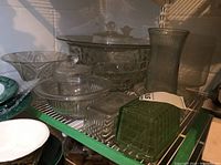 Shelf view showing the punch bowl, trifle bowl, ribbed vase, and various lidded and open bowls stacked on a shelf.