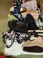 Overview of assorted handbags and backpacks arranged inside and on top of a white wire basket showing variety of colors and styles.