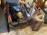 Two large plastic lidded bins filled with various knitting and sewing supplies such as yarn balls, knitting needles, and bags, alongside a folding wooden frame.