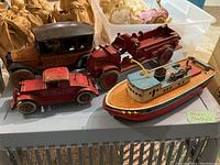 Four metal toy vehicles and a boat on a gray surface with a laundry basket in background; shows overall contents and condition.
