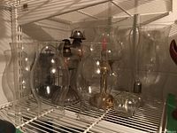 Photo showing two oil lamps with glass hurricane shades, three spare hurricane glass shades, two mini oil lamps, a candle holder lamp with brass-style base and glass shade, and a lantern-style lamp.