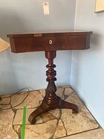 Side view of the wooden pedestal sewing table showing the carved base and keyhole on front.