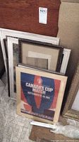 Collection of framed posters and prints stacked against a wall, showing variety in frame color and size.