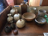 Collection of pottery bowls, mugs, and vases displayed on a wooden surface including various shapes and finishes.