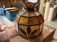 Front and side of hexagonal stained glass swag light showing amber, cream, red and green glass panels and metal frame.