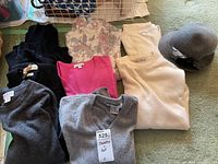 Photo showing six cashmere sweaters in black, dark gray, light gray, pink, cream, and floral pattern along with a gray felt ladies hat with flower decoration.