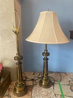 Full view of both matching heavy metal base table lamps next to each other, one with shade and one without.