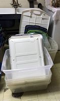 Nine various sized plastic storage totes stacked with lids in colors white, green, and dark blue