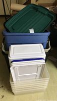 Stack of assorted plastic totes with lids in varying sizes and colors, some lids mismatched.