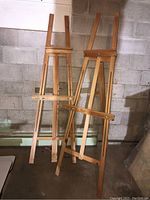 Photo of two wooden easels standing side by side against a concrete wall, showing overall structure and height.