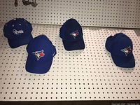 Front view of four caps showing logos: three Blue Jays hats and one Ropes hat with tags.