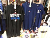 Three men's Toronto Blue Jays shirts on hangers against a pegboard, displaying different blue and black designs with logos and text.