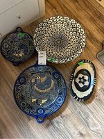 Five decorative bowls displayed on wooden floor including large terracotta bowls with floral patterns and dark blue peacock motif bowls.