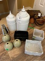 White ceramic lidded jars, assorted vases, planters and containers placed on wooden floor