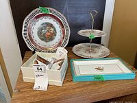 Lot with decorative china plate, two-tiered floral serving stand, rectangular platter with animal motif, white box with demitasse cup and saucer inside, blue trimmed rectangular plate, and plate stand