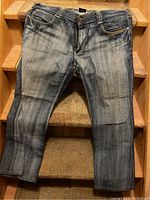 Front view of a pair of blue SUKO jeans laid flat on stairs, showing button closure and pockets.