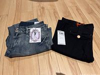 Two folded pairs of jeans, blue denim Suko size 8 with tags, and black Earnest Sewn size 31 with tag