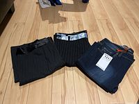 Three pairs of ladies' pants arranged on floor: two black pinstripe pants and one blue denim jeans with tags.