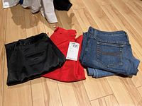 Four pairs of ladies pants including two pairs of jeans and two pairs of dress pants folded on wooden floor.