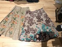 Two ladies skirts side by side; left skirt beige with floral embroidery and the right skirt grey with brown and turquoise embroidery
