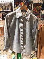 Front view of gray suede shirt hanging on wooden hanger showing button-up design.