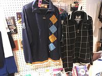 Two men's full zip jackets on hangers; navy PMB jacket with argyle pattern on left, black Death Valley jacket with grid pattern and skull graphic on right.