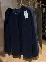 Three men's long-sleeved shirts hanging on white hangers including a navy blue Sportek shirt with visible logo.