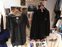 View of the ladies' Roots hoodie (gray, V-neck, three-quarter sleeves) and the men's black zippered fleece with NFL Buccaneers logo, both hanging on hangers.