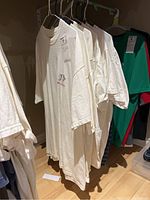 Seven men's t-shirts hanging on hangers in basement, mostly white with one green/red shirt, some show discoloration.