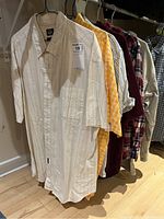 View of six men's button-up shirts on hangers including white Dockers shirt with vertical stripes and other colored shirts